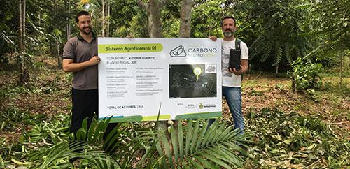Duas pessoas segunrando uma placa sobre o projeto carbono neutro